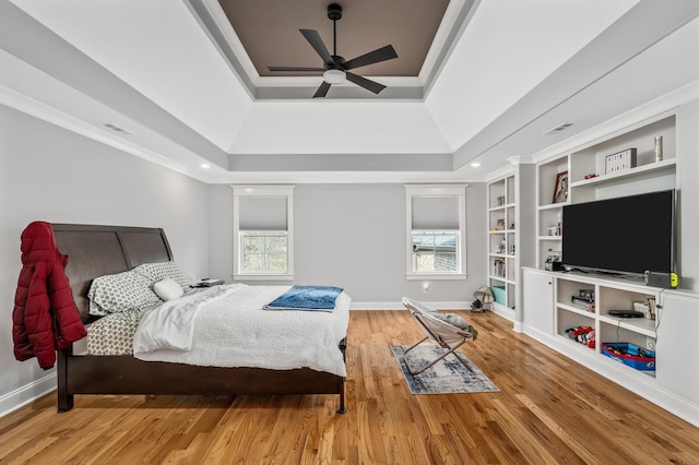 bedroom featuring crown molding, a raised ceiling, visible vents, wood finished floors, and baseboards