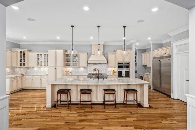 kitchen featuring a large island, appliances with stainless steel finishes, a breakfast bar, cream cabinets, and light wood-style floors