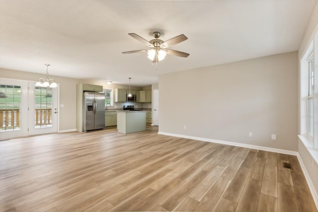 unfurnished living room featuring ceiling fan with notable chandelier, light wood-type flooring, and baseboards