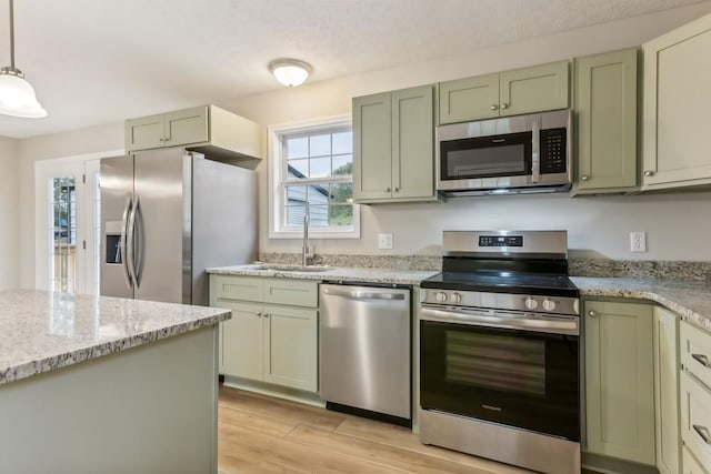 kitchen with light stone counters, light wood finished floors, appliances with stainless steel finishes, a sink, and green cabinetry