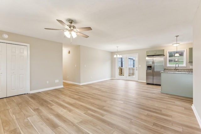 unfurnished living room with baseboards, a sink, light wood finished floors, and ceiling fan with notable chandelier