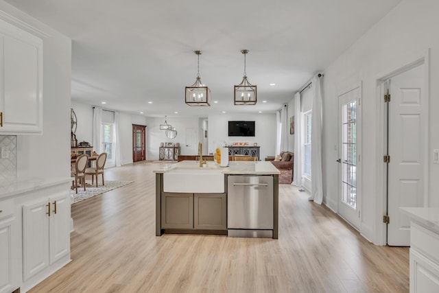 kitchen featuring open floor plan, stainless steel dishwasher, a sink, and light wood-style flooring