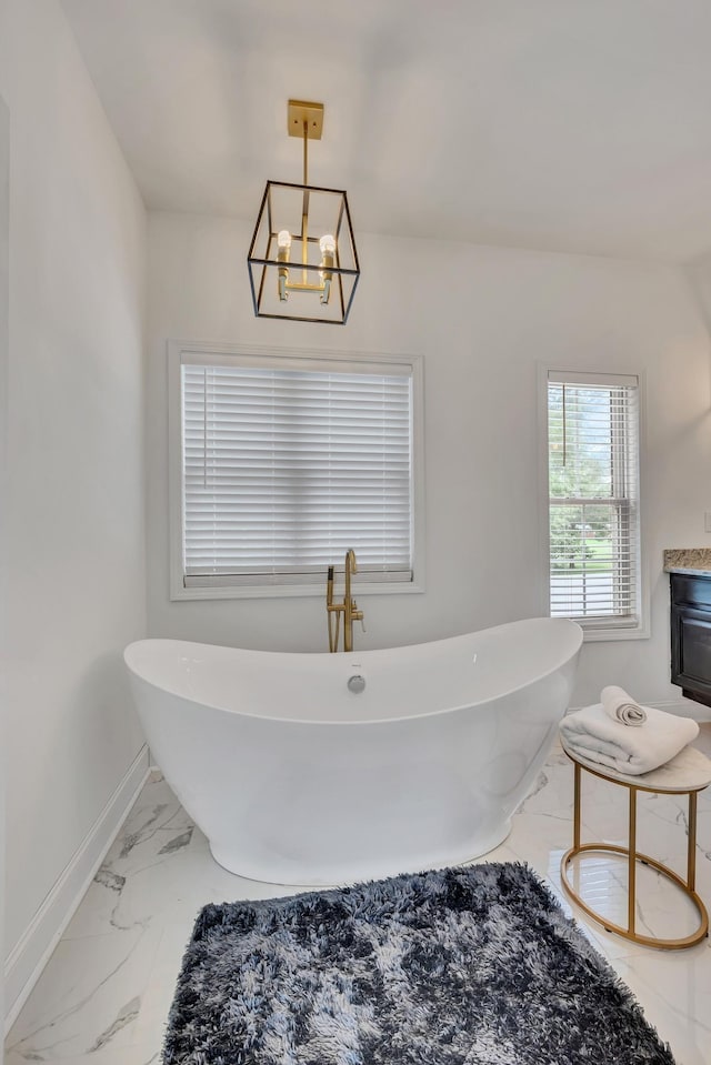 bathroom featuring a freestanding bath, marble finish floor, a notable chandelier, and baseboards