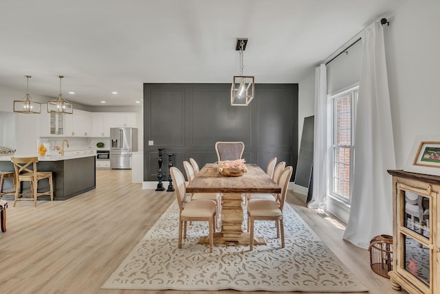 dining room with recessed lighting, a decorative wall, and light wood finished floors