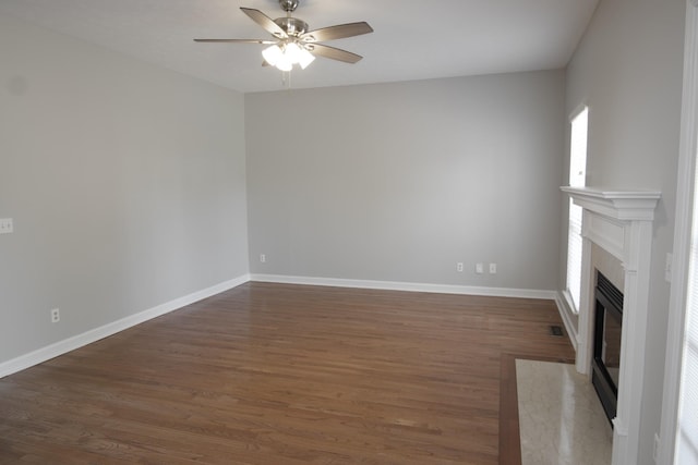 unfurnished living room with ceiling fan, baseboards, wood finished floors, and a high end fireplace