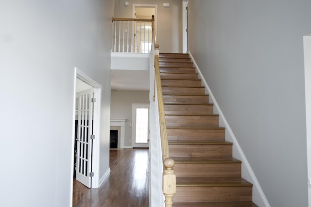 stairway featuring a fireplace with flush hearth, a high ceiling, baseboards, and wood finished floors