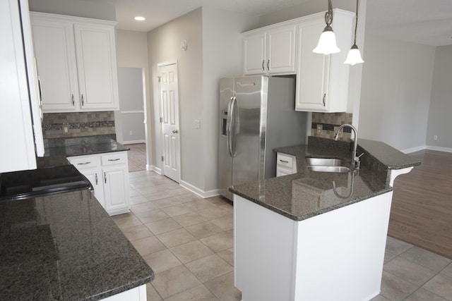 kitchen featuring a peninsula, a sink, white cabinetry, backsplash, and stainless steel fridge