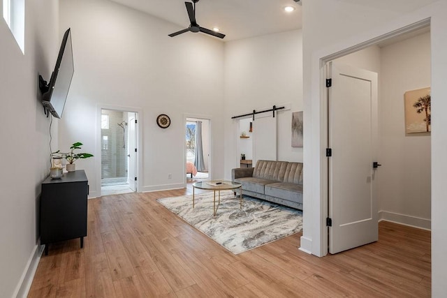 living room featuring a ceiling fan, light wood-style flooring, baseboards, and a barn door