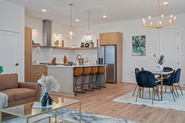 kitchen featuring tasteful backsplash, light wood-style flooring, a breakfast bar area, extractor fan, and stainless steel refrigerator with ice dispenser