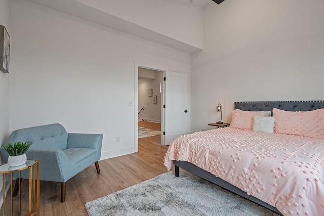 bedroom featuring a high ceiling, light wood-style flooring, and baseboards