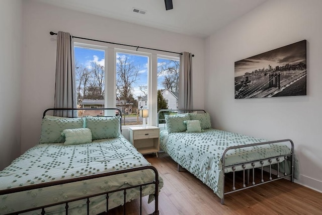 bedroom featuring a ceiling fan, wood finished floors, visible vents, and baseboards