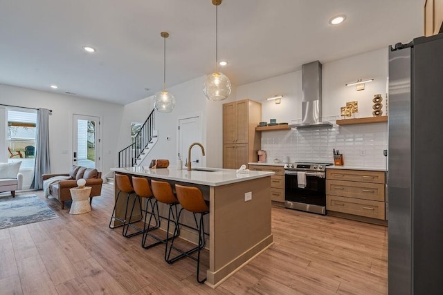 kitchen with a breakfast bar area, open shelves, appliances with stainless steel finishes, a sink, and wall chimney range hood