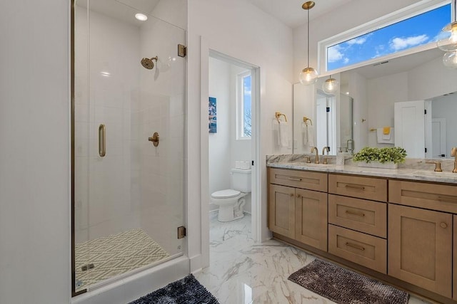 bathroom featuring toilet, a sink, marble finish floor, a shower stall, and double vanity