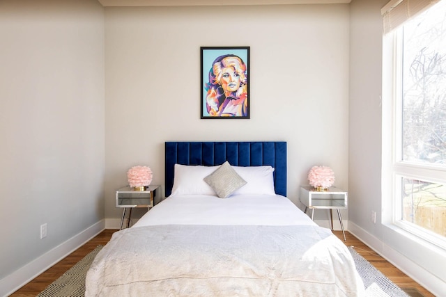 bedroom with multiple windows, wood finished floors, and baseboards