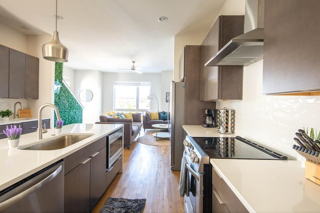 kitchen with wall chimney exhaust hood, appliances with stainless steel finishes, open floor plan, light countertops, and a sink