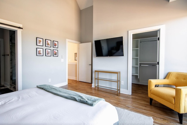 bedroom with wood finished floors, a walk in closet, a high ceiling, and baseboards