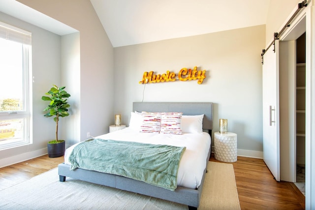 bedroom with lofted ceiling, a barn door, baseboards, and wood finished floors