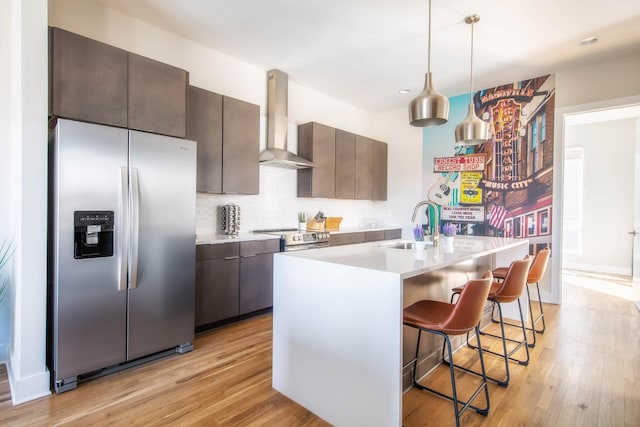 kitchen featuring light wood finished floors, wall chimney exhaust hood, stainless steel appliances, and a sink