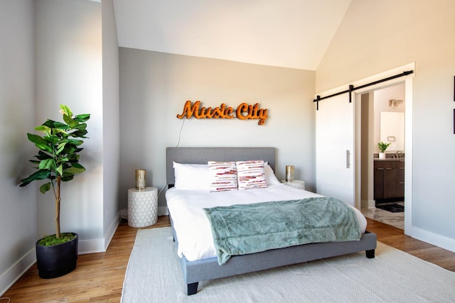 bedroom with a barn door, baseboards, vaulted ceiling, and wood finished floors