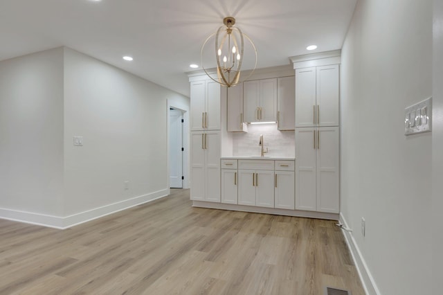 kitchen with light wood-style flooring, a sink, baseboards, light countertops, and backsplash