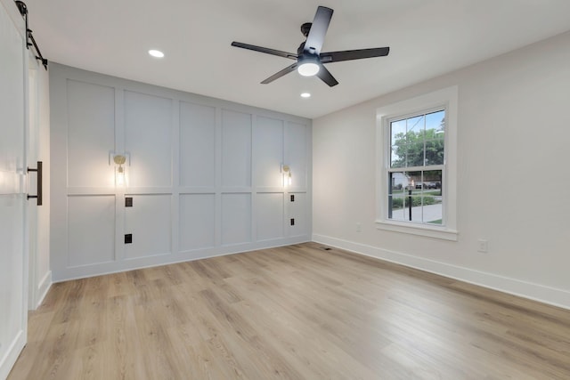 unfurnished bedroom featuring light wood finished floors, a barn door, baseboards, and a decorative wall