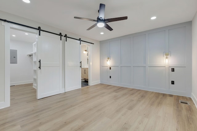 unfurnished bedroom with a barn door, electric panel, visible vents, and a decorative wall