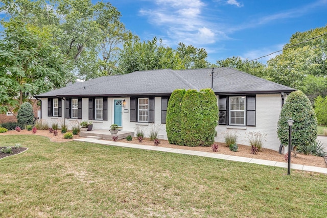 single story home featuring brick siding, a shingled roof, and a front yard