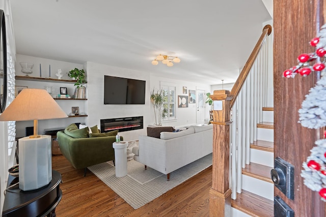 living area with stairway, wood finished floors, and a glass covered fireplace