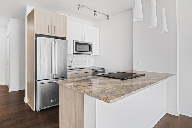 kitchen with a peninsula, dark wood-type flooring, a sink, appliances with stainless steel finishes, and tasteful backsplash