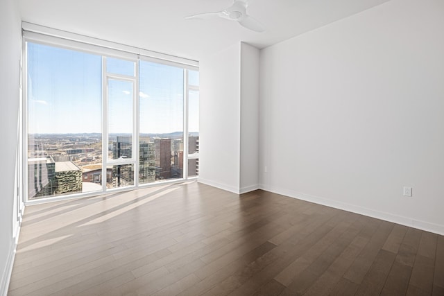 unfurnished room with ceiling fan, baseboards, dark wood finished floors, and a wall of windows