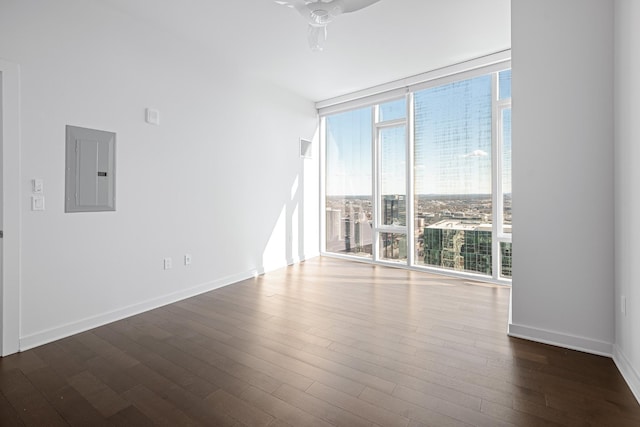 unfurnished room with a ceiling fan, baseboards, electric panel, floor to ceiling windows, and dark wood finished floors