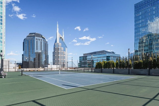 view of tennis court featuring community basketball court, fence, and a city view