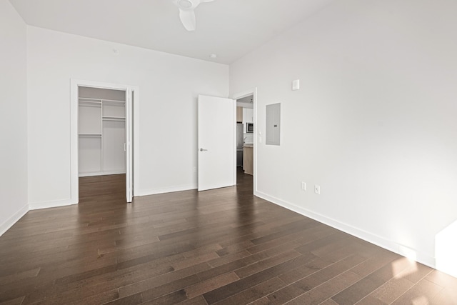 unfurnished bedroom featuring electric panel, baseboards, dark wood-style flooring, a walk in closet, and a closet