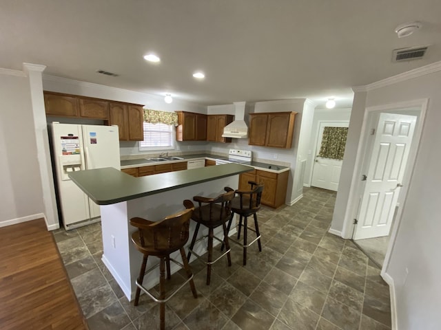 kitchen with wall chimney exhaust hood, white appliances, a kitchen island, and visible vents