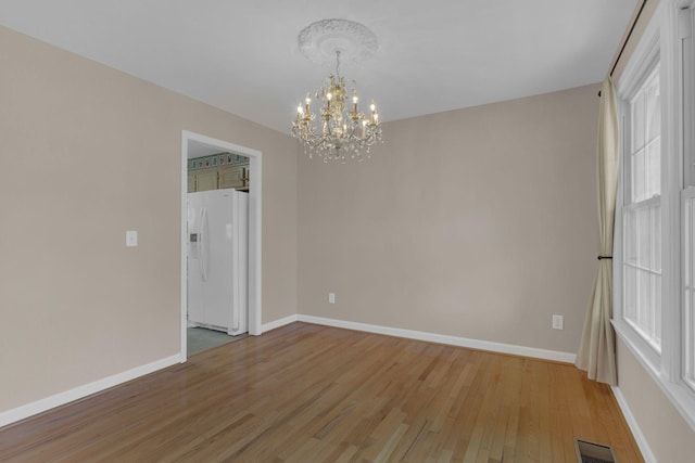 empty room with light wood-type flooring, an inviting chandelier, baseboards, and visible vents