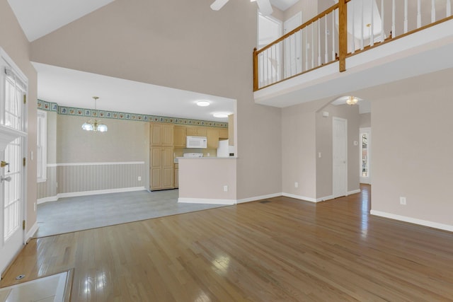 unfurnished living room with a towering ceiling, light wood finished floors, baseboards, and ceiling fan with notable chandelier