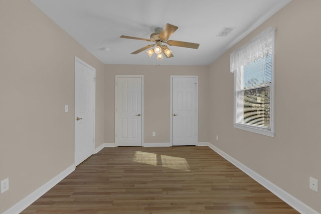 unfurnished bedroom with a ceiling fan, baseboards, visible vents, and wood finished floors