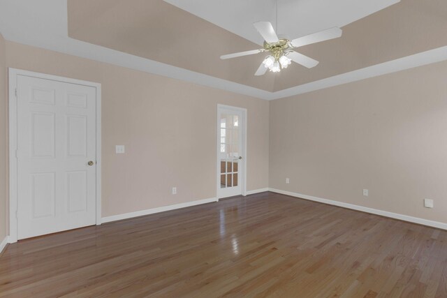 empty room featuring baseboards, a tray ceiling, and wood finished floors