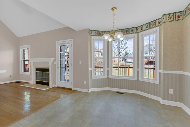 unfurnished dining area featuring baseboards, an inviting chandelier, a glass covered fireplace, and wallpapered walls