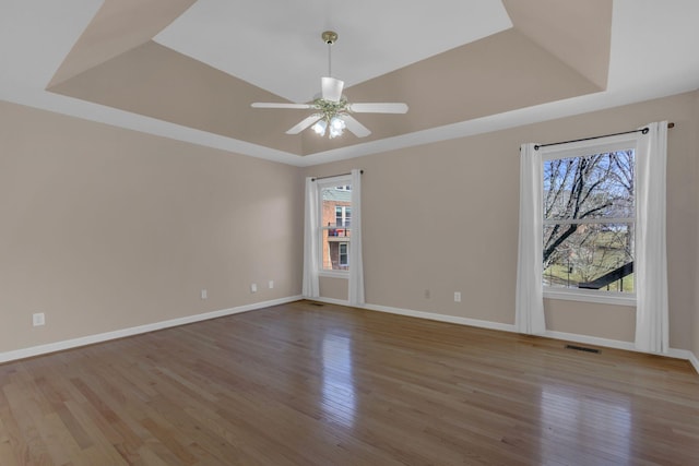 empty room featuring baseboards, visible vents, a tray ceiling, and wood finished floors