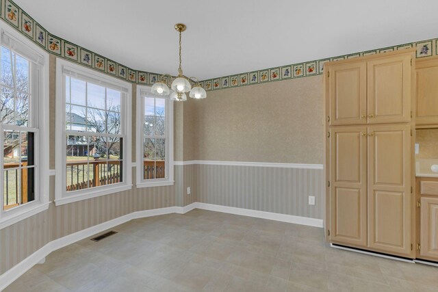 unfurnished dining area with wallpapered walls, baseboards, visible vents, and a notable chandelier