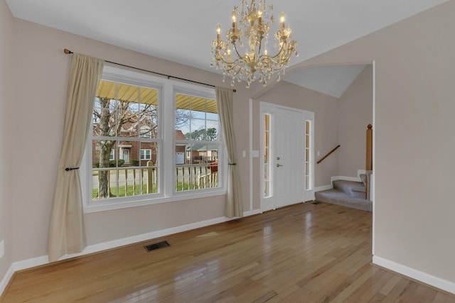 foyer featuring baseboards, visible vents, stairway, wood finished floors, and an inviting chandelier