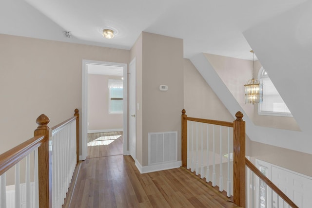 hallway with wood finished floors, an upstairs landing, visible vents, and an inviting chandelier