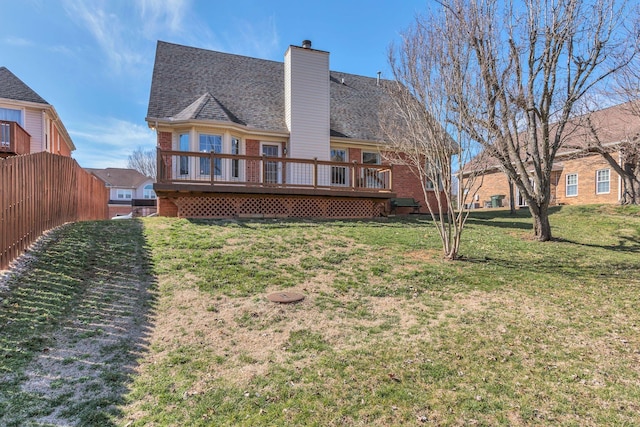 back of property with a deck, brick siding, roof with shingles, a lawn, and a chimney