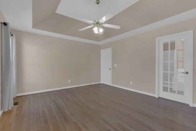 unfurnished room featuring a ceiling fan, baseboards, a tray ceiling, and wood finished floors