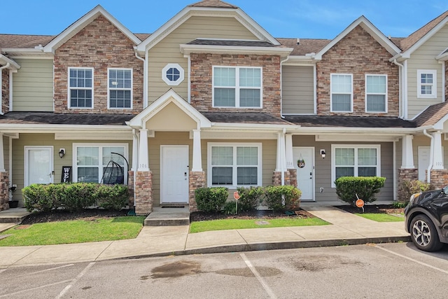 townhome / multi-family property featuring uncovered parking, stone siding, and roof with shingles