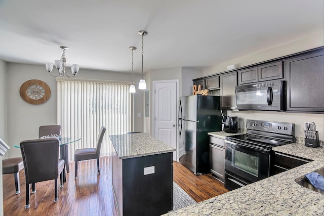 kitchen featuring light stone counters, dark wood-type flooring, hanging light fixtures, and black appliances