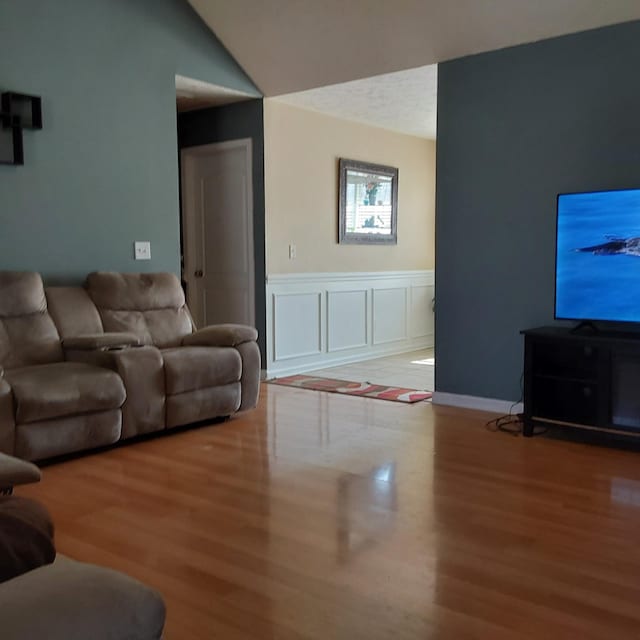 living area featuring lofted ceiling, wainscoting, wood finished floors, and a decorative wall