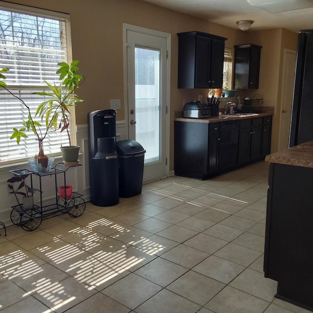 kitchen featuring light tile patterned floors, light countertops, a sink, dark cabinets, and black fridge