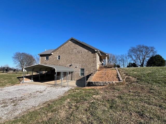 view of side of home with gravel driveway, a yard, and a detached carport